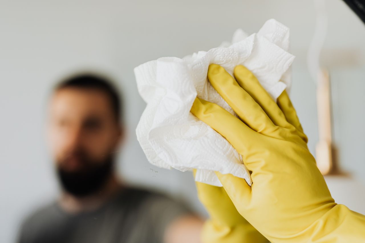 why-choose-us Unrecognizable bearded male wearing yellow latex gloves wiping mirror with napkin in bathroom at home